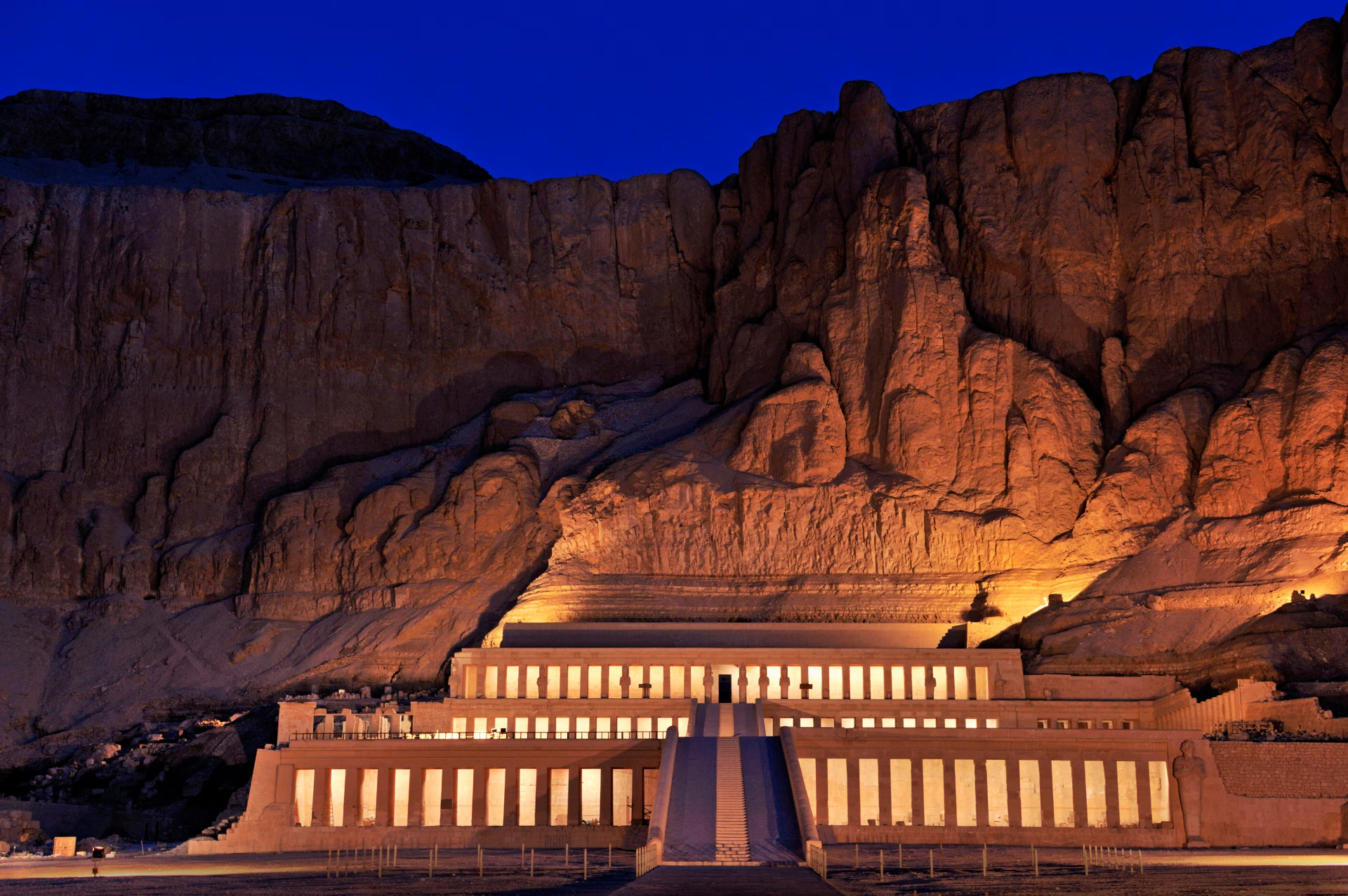 Hatshepsut temple illuminated at dusk beneath towering desert cliffs.