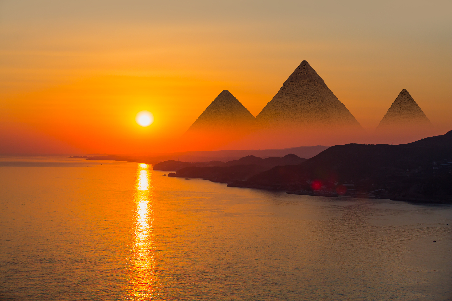 Sunset over pyramids with sun reflecting on water