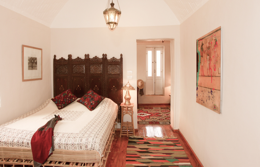 Marsam Hotel room with carved wooden headboard, lantern, and woven kilim rugs on warm wood floors.