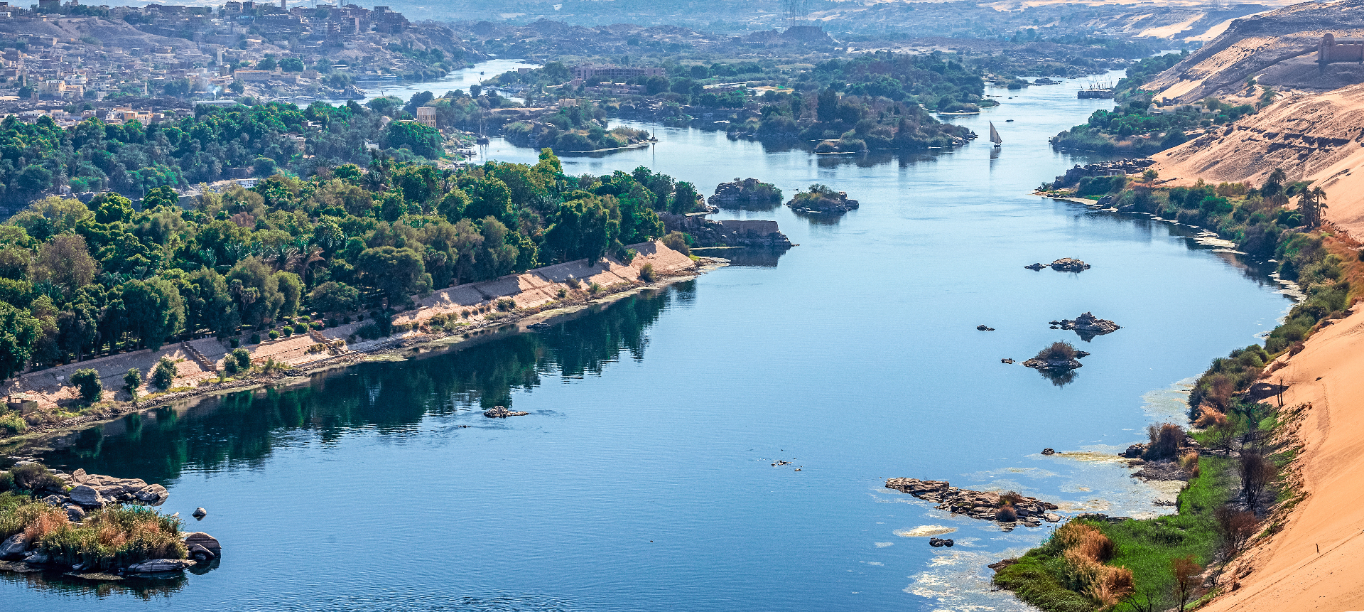 Aerial view of the Nile river winding through Aswan with green islands and desert dunes.